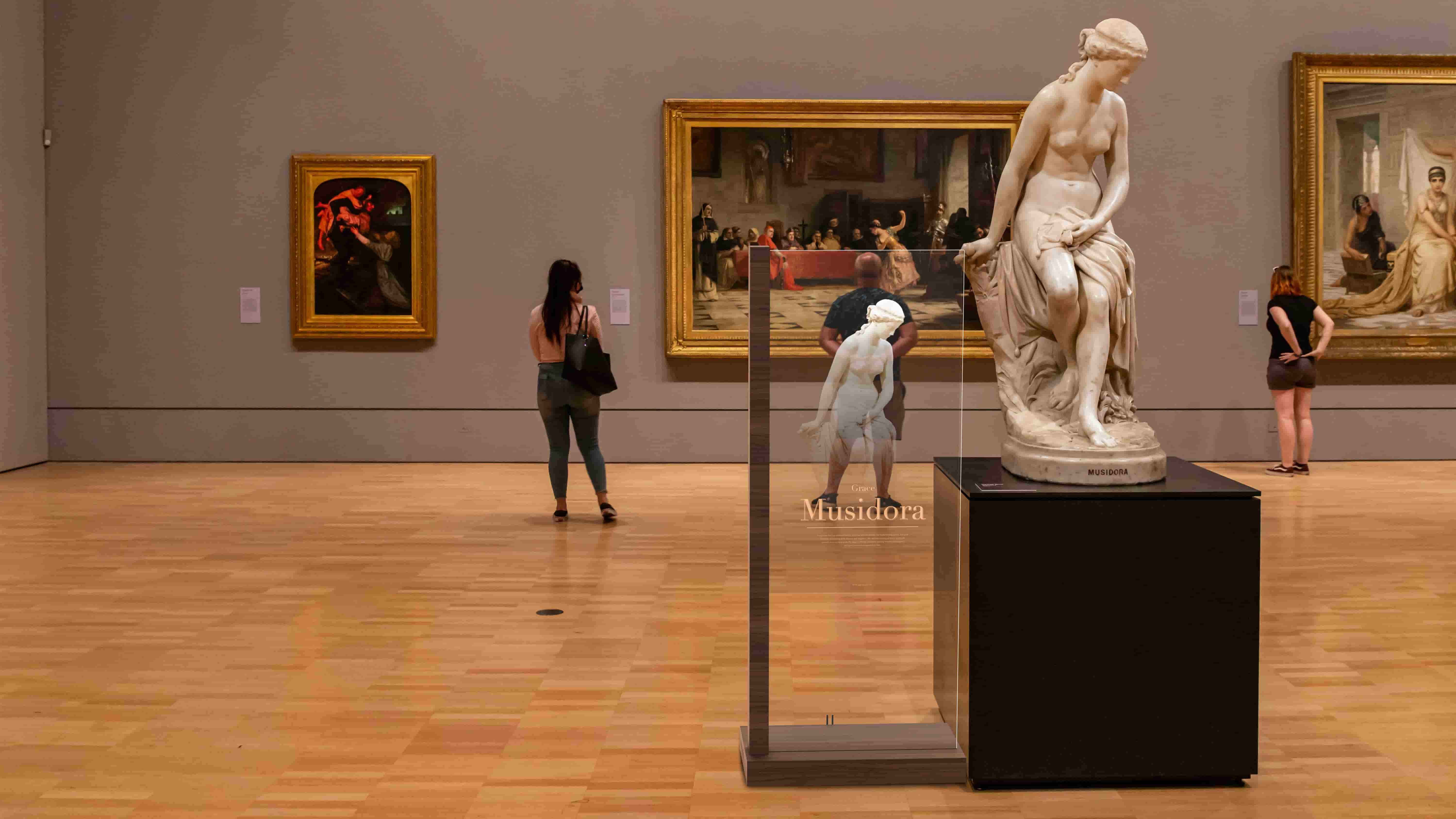Transparent OLED display kiosk showcasing dynamic graphics in front of a museum sculpture exhibit