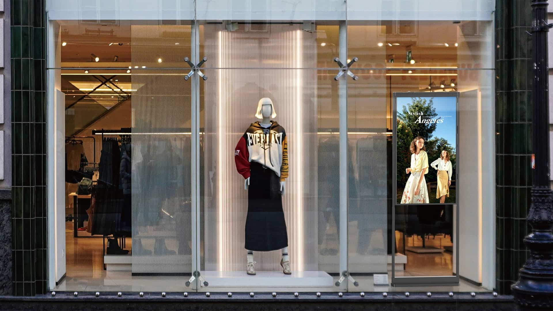 Window-facing digital display showing fashion advertising behind the glass of a street-facing clothing store